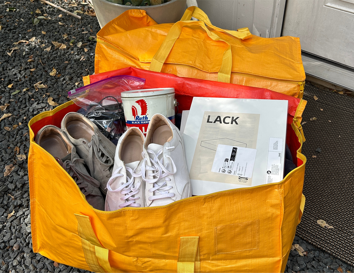 Yellow tote bag filled with shoes, a coffee cup, and a box on a gravel surface.