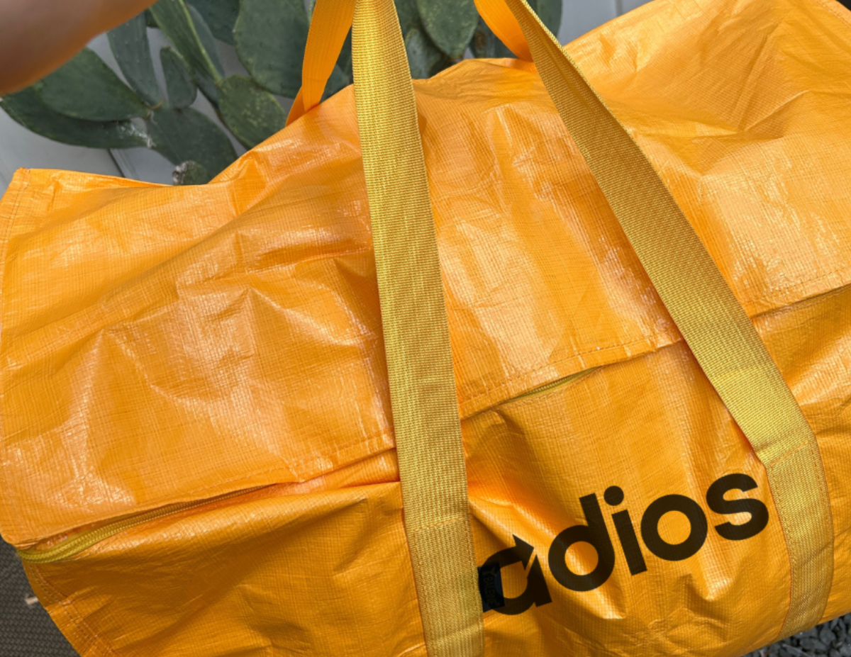 Yellow duffel bag with 'Adios' logo on a blurred background