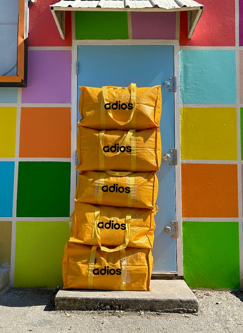 Stack of yellow bags with 'adios' text against a colorful geometric-patterned wall.