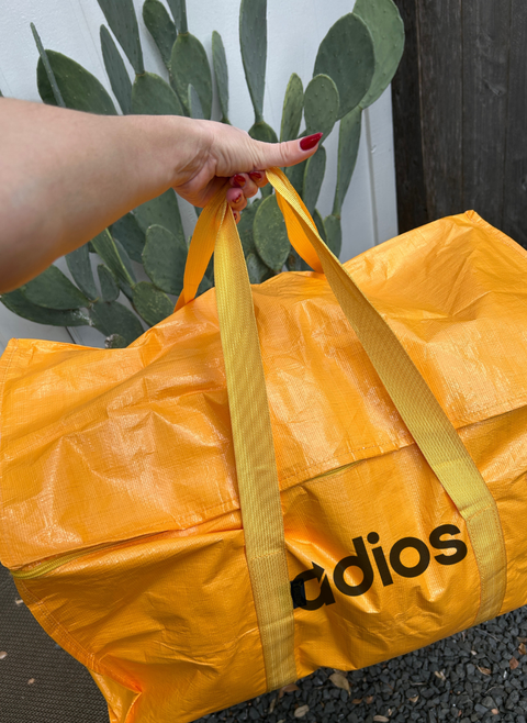 Person holding a yellow 'adios' bag with a plant in the background