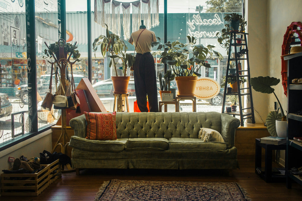 Green sofa with orange cushions in a store setting with large windows.