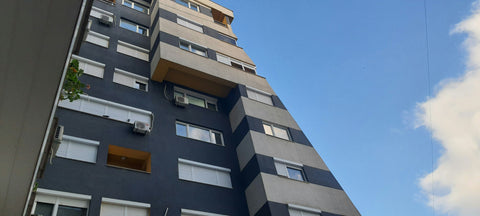 Tall apartment building with a blue and gray facade against a clear sky.