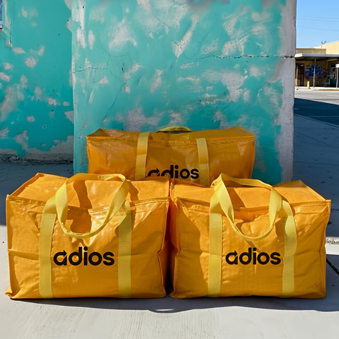 Three yellow bags with 'adios' branding against a textured blue wall.