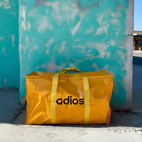 Yellow bag with 'adios' branding against a textured blue wall.